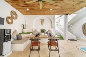A modern dining area with a central table, two chairs, a water dispenser, and a seating bench. - Casa Sud Villa - Modern 3BR w Pool, Outdoor Lounge & Beach Access (Kabupaten Badung)