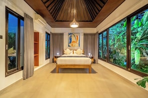 Ein Schlafzimmer mit einem großen Bett, einem Deckenventilator und Blick ins Grüne durch die Fenster.