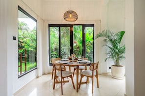 Uma sala de jantar com mesa redonda, quatro cadeiras e uma grande janela com vista para o verde.