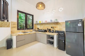 A modern kitchen with a built-in stove, a refrigerator, and a window with a view of greenery. - New 2BR Villa in Modern Ubud Complex w Spa+2 Pools (Ubud)