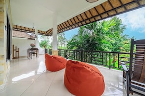 Varanda ampla com vista para vegetação exuberante, área de refeições com mesa e cadeiras, e dois bean bags.