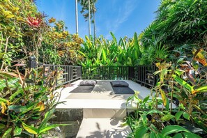 A garden with a seating area, surrounded by lush tropical plants and palm trees. - Chic 2BR Villa in Calm Ubud Complex w Spa+2 Pools (Kabupaten Gianyar)