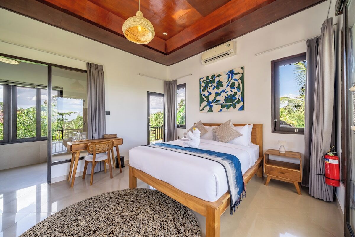 Quarto com cama, mesa de cabeceira e vista para o exterior.