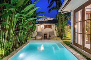 Ein Pool mit zwei Liegestühlen und einem Tisch, umgeben von tropischen Pflanzen.