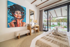 A hotel room with a large painting, a desk, a bench, a bed, and a view of the outdoor area. - Designer 3BR Villa w Garden Bath & Pool • Ubud (Gianyar Regency)