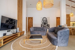 A modern living room with a flat-screen TV, grey sofas, a coffee table, and a woven rug. - Designer 3BR Villa w Garden Bath & Pool • Ubud (Gianyar Regency)