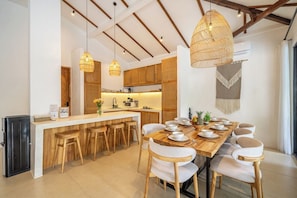 A modern kitchen with wooden cabinets, a central island with stools, and pendant lighting. - Designer 3BR Villa w Garden Bath & Pool • Ubud (Gianyar Regency)
