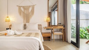 A bedroom with a bed, bedside table, chair, and a desk with a mirror. There is a window with curtains and a view of greenery outside. - Designer 3BR Villa w Garden Bath & Pool • Ubud (Gianyar Regency)