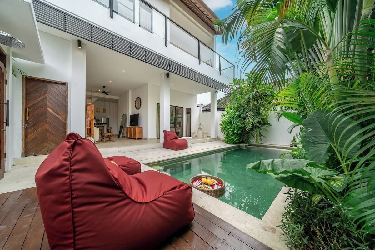 Une maison moderne avec une piscine, des fauteuils en forme de haricot rouge et une végétation luxuriante.