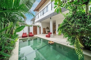 Ein modernes Haus mit Pool mit Glasboden, umgeben von üppiger Vegetation und einem zweistöckigen Gebäude.