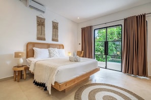 Une chambre avec un grand lit, une petite table de chevet, une lampe et une vue sur la verdure grâce à une porte coulissante.