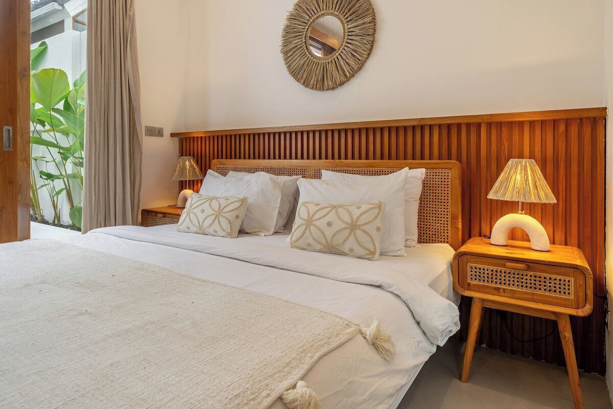 A bedroom with a wooden headboard, a bed with white bedding, two bedside lamps, and a wall-mounted mirror.