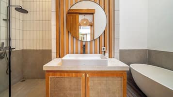 Een badkamer met een vrijstaand bad, een wastafel met een houten opbergmeubel en een douche met een regendouchekop.