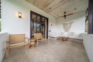 A covered outdoor seating area with a wooden ceiling, a white wall, and a white sofa. - Putri Salju - Tropical 2BR Villa w Huge Garden+Patio • Lush Ubud (Kabupaten Gianyar)