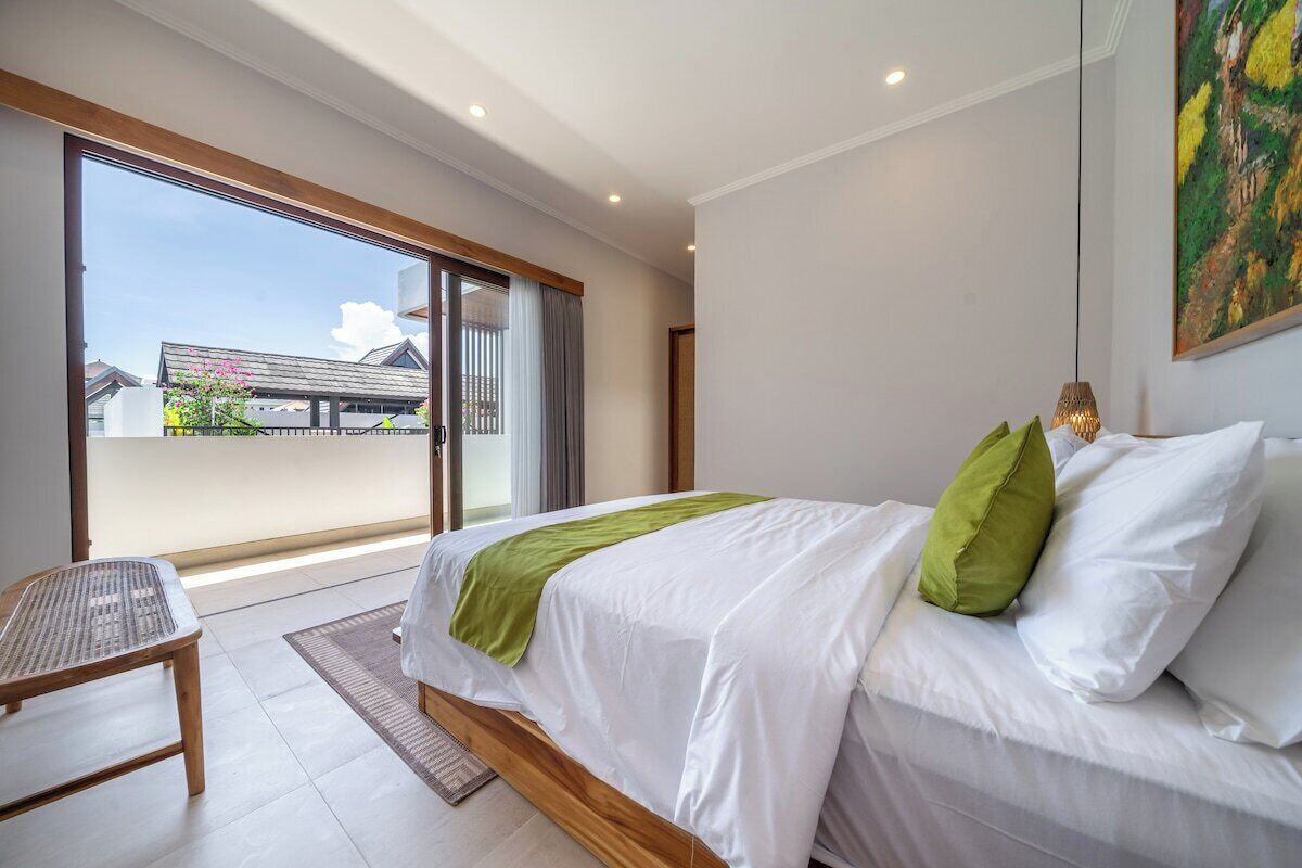 A bedroom with a bed, a bench, and a view of buildings through a sliding door.