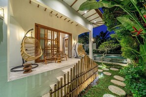 A modern outdoor seating area with wicker chairs, a bamboo fence, and a stone pathway leading to a pool. - Unique 2BR Villa w Outdoor Bath, Pool+Huge Garden (Kabupaten Gianyar)