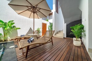 A wooden deck with lounge chairs and an umbrella, surrounded by potted plants and a small pool. - Chic 3BR in Prime Sanur w Pool & Beach Access (Kota Denpasar)