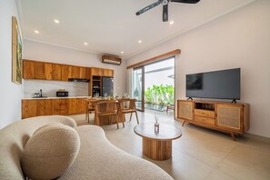 A modern living room with a sofa, a coffee table, and a television. - Chic 3BR in Prime Sanur w Pool & Beach Access (Kota Denpasar)