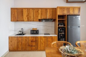 A kitchen with wooden cabinets, a marble countertop, a black microwave, a coffee maker, a black refrigerator, and a dining table with chairs. - Chic 3BR in Prime Sanur w Pool & Beach Access (Kota Denpasar)