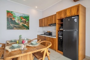 A modern kitchen with wooden cabinets, a black refrigerator, and a dining table set with plates and glasses. - Chic 3BR in Prime Sanur w Pool & Beach Access (Kota Denpasar)