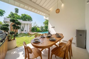 Zona d'exterior per dinar amb taula de fusta preparada per a quatre persones, amb cadires al voltant, una barbacoa i plantes en testos a prop.