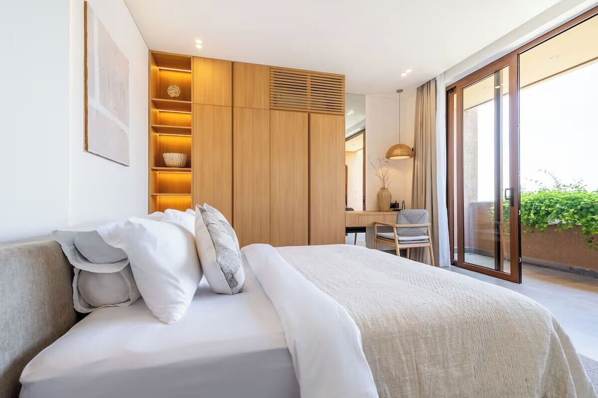 Une chambre moderne avec un grand lit, une armoire intégrée, un bureau et un balcon agrémenté de plantes.