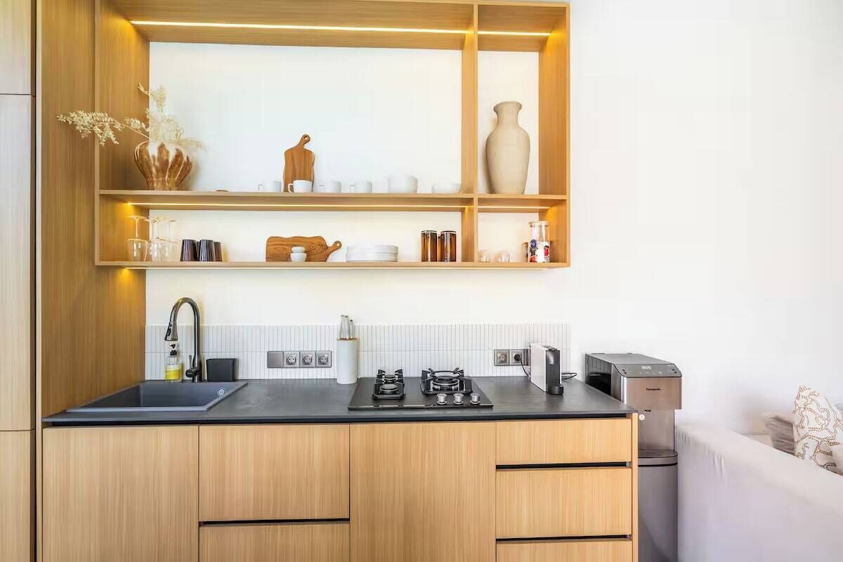Une cuisine moderne avec des meubles en bois, un plan de travail noir et une étagère intégrée au-dessus de l’évier.