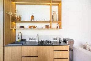 Une cuisine moderne avec des meubles en bois, un plan de travail noir et une étagère intégrée au-dessus de l’évier.