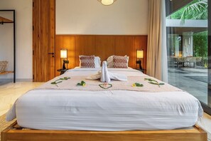 Een hotelkamer met een groot bed, twee nachtkastjes met lampen, een houten hoofdeinde en uitzicht op een buitenruimte.