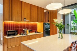 A modern kitchen with wooden cabinets, a microwave, a kettle, and a vase with flowers on the island. - X7 Ubud - Tropical Ubud's 3BR Gem w Pool & Outdoor Dining (Gianyar Regency)