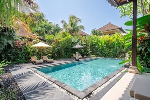 A swimming pool surrounded by lush greenery, with lounge chairs and umbrellas. - Serene 2BR Villa in Ubud Complex w Spa & 2 Pools (Kabupaten Gianyar)