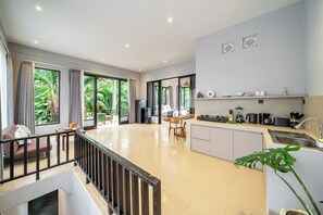 A modern kitchen with a dining area, large windows, and a view of greenery. - Serene 2BR Villa in Ubud Complex w Spa & 2 Pools (Kabupaten Gianyar)