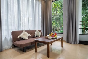 A room with a sofa, a wooden table with fruit, and a view of greenery outside. - Serene 2BR Villa in Ubud Complex w Spa & 2 Pools (Kabupaten Gianyar)