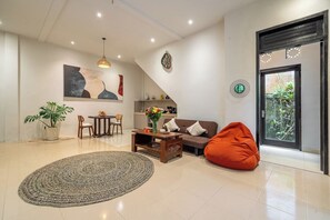 A modern living room with a sofa, a coffee table, a red bean bag, a dining area with chairs, a potted plant, and a large abstract painting on the wall. - Serene 2BR Villa in Ubud Complex w Spa & 2 Pools (Kabupaten Gianyar)