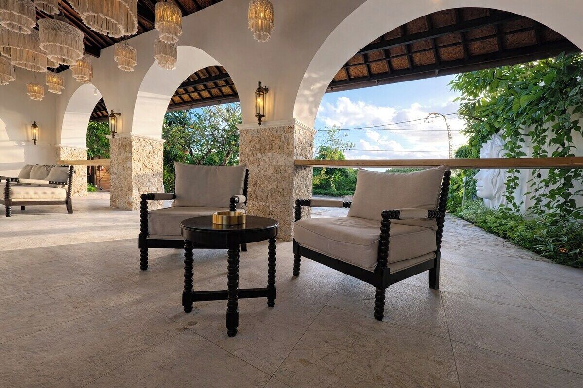 An outdoor seating area with stone pillars, cushioned chairs, and a round table.