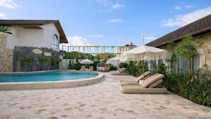 Zona de piscina con sillones de descanso y sombrillas, rodeada de muros de piedra y vegetación.