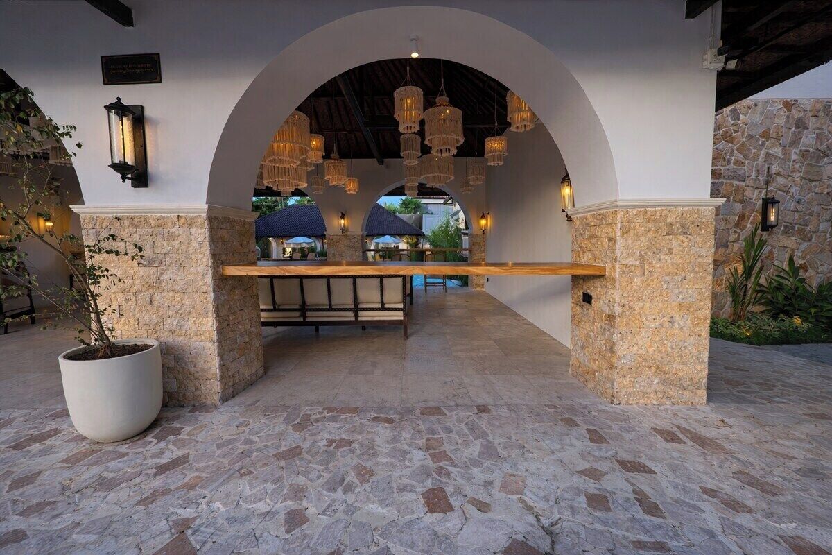 Patio esterno con pavimento in pietra, una panca di legno e lampade a sospensione.