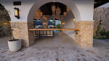 Patio esterno con pavimento in pietra, una panca di legno e lampade a sospensione.
