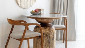 Un coin repas minimaliste avec une table ronde, deux chaises en bois et une décoration murale en macramé.