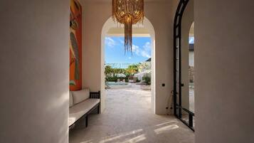 A hallway leading to an outdoor area with a pool, a bench, and a large painting on the wall.