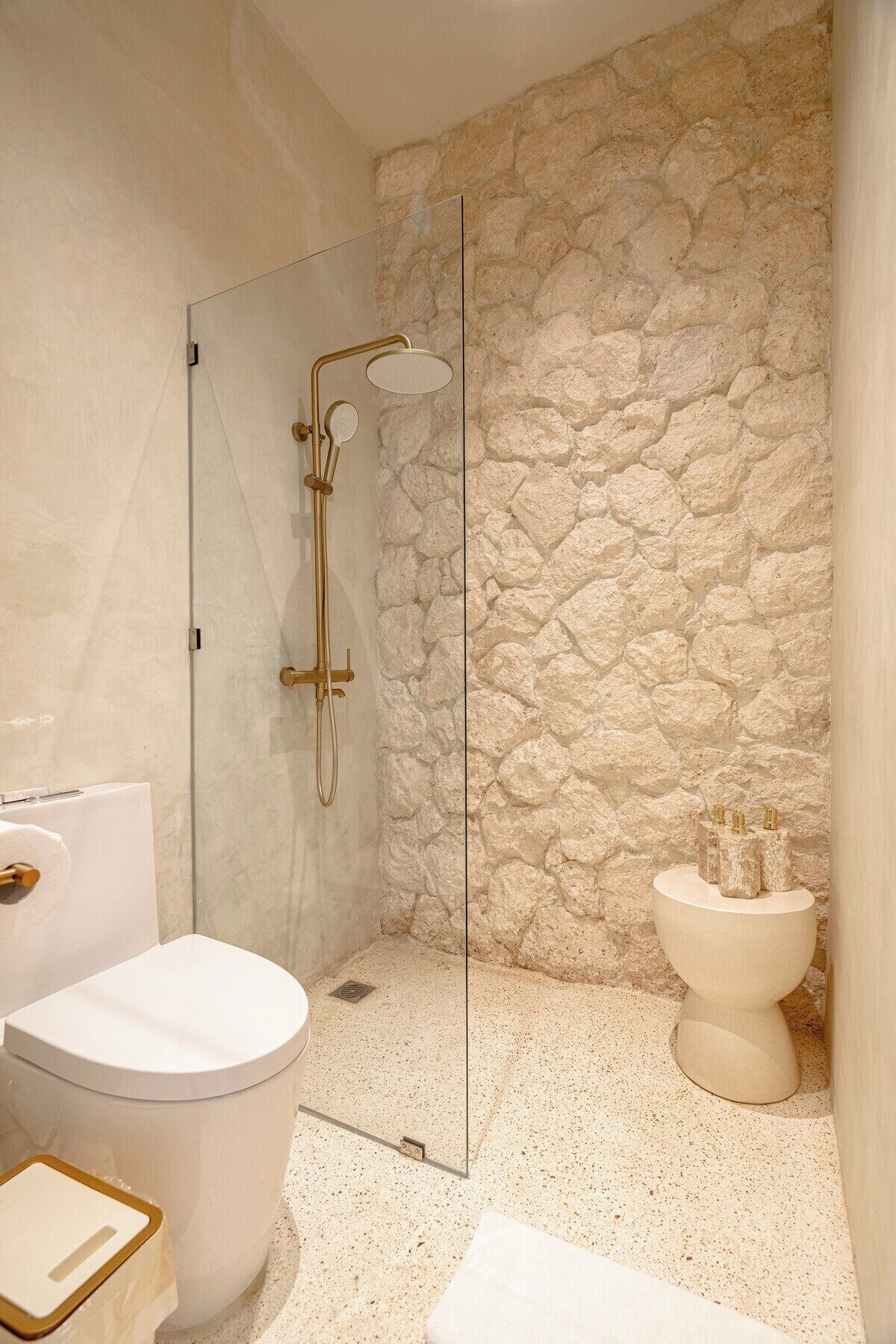 A bathroom with a stone wall, a glass shower enclosure, a toilet, and a bathtub.