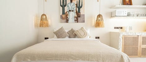 Une chambre avec un grand lit, une œuvre d’art accrochée au mur, une lampe suspendue et une étagère avec divers objets.