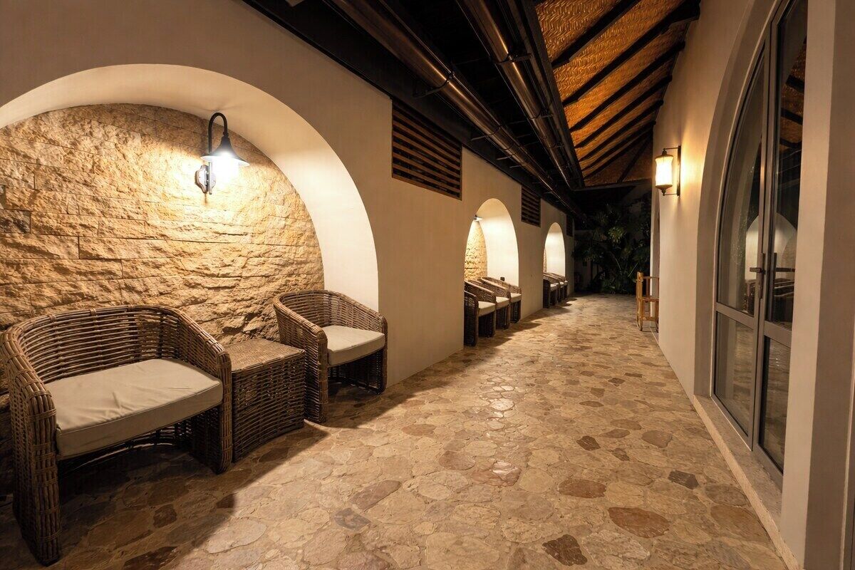 Un pasillo con suelo de piedra, muebles de mimbre y arcos con iluminación.