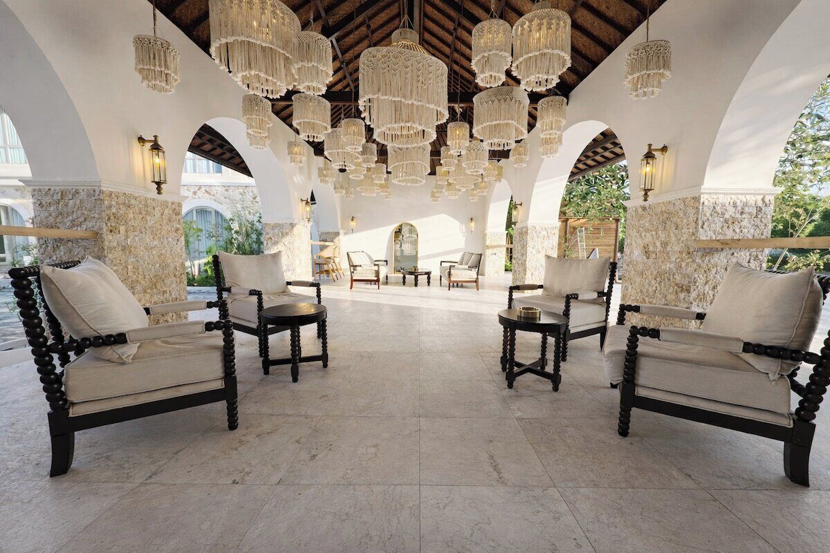 A spacious lounge area with multiple sofas and tables, ornate chandeliers, and a stone wall backdrop.