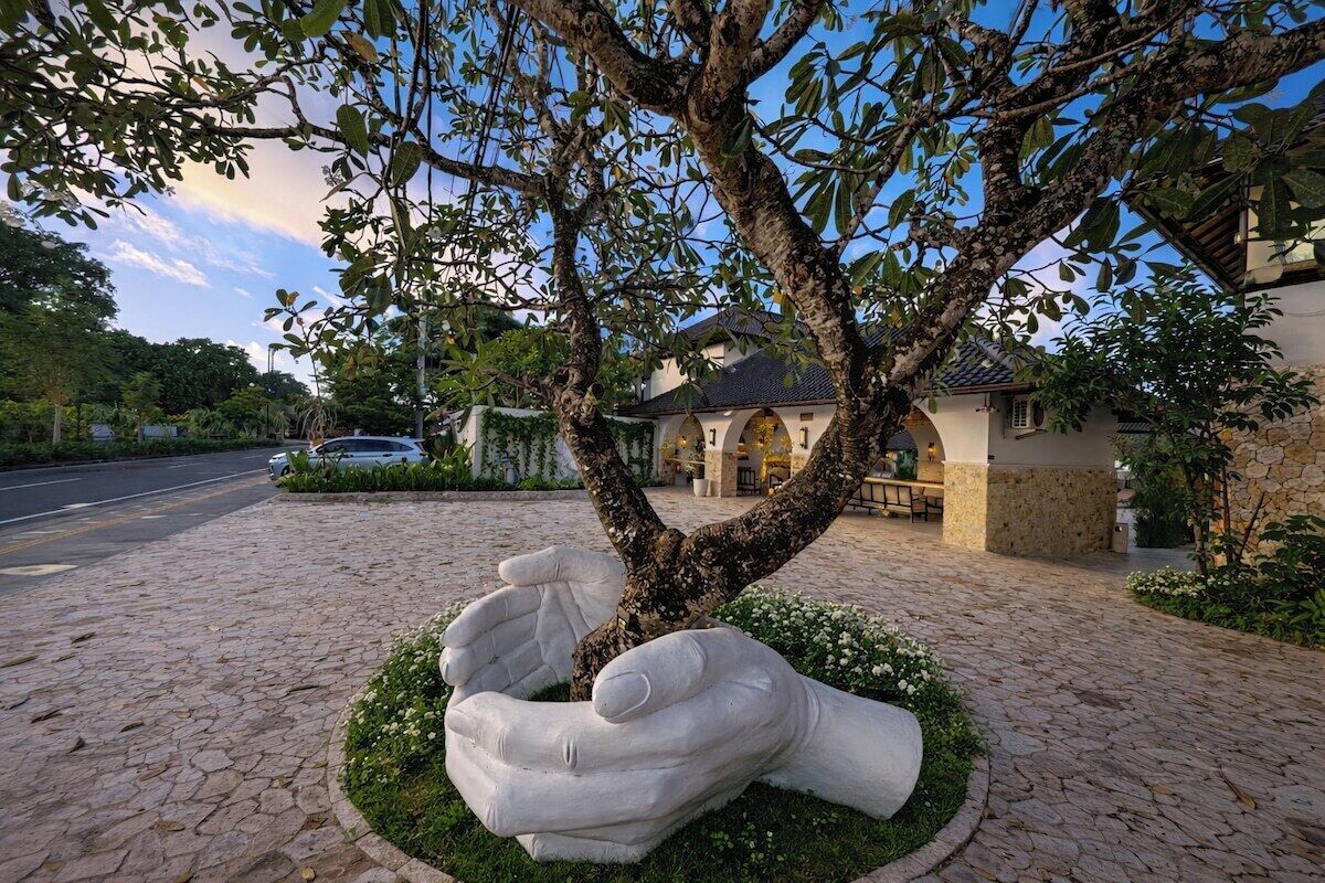 A tree with a sculpture of two hands embracing in a circular garden bed.