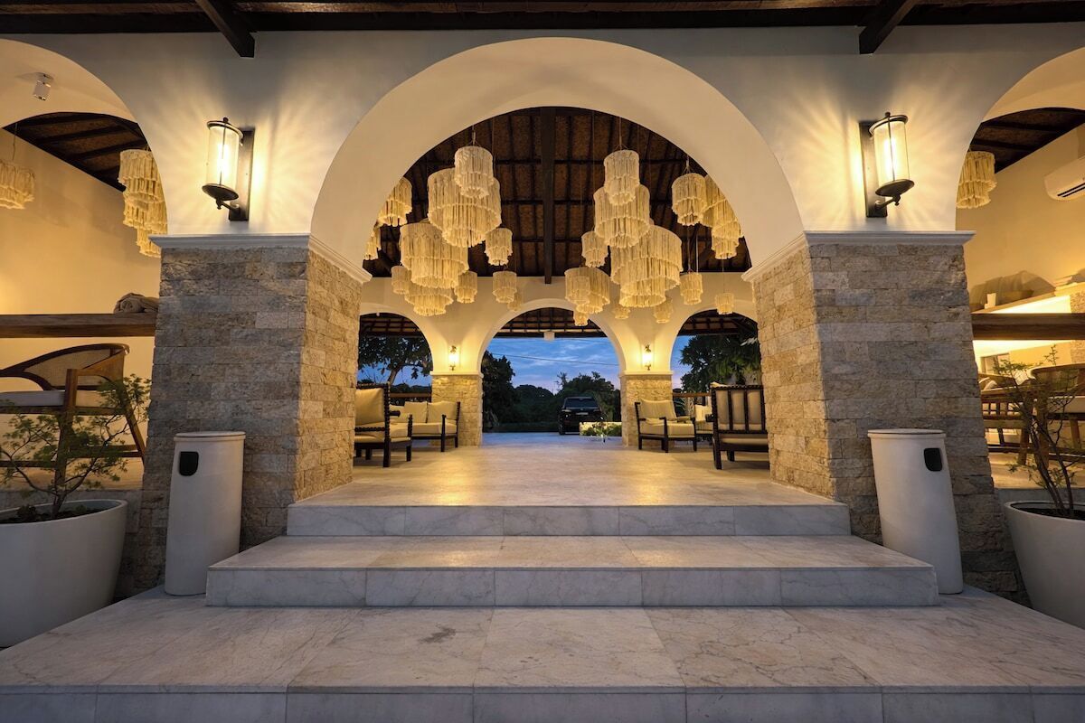 An outdoor covered area with stone pillars, multiple seating arrangements, and hanging chandeliers.