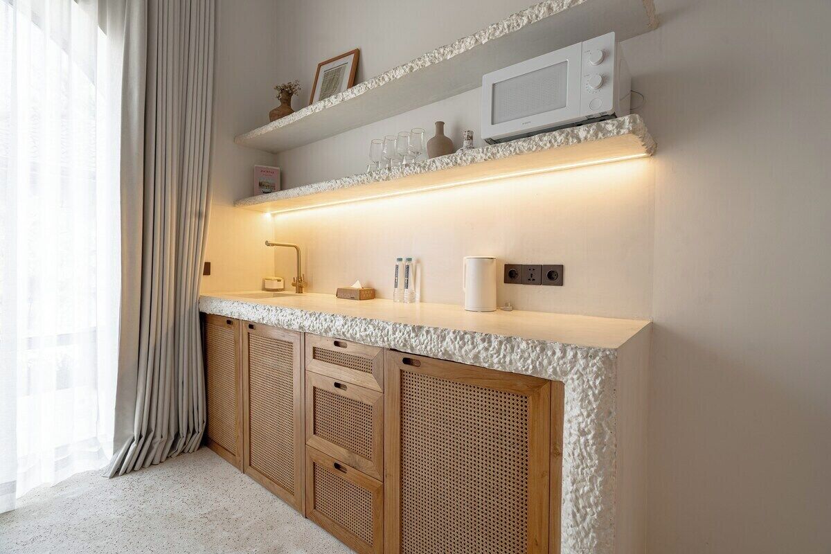 A kitchen with a white countertop, wooden cabinets, and a microwave on a shelf.