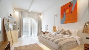 Ein Schlafzimmer mit einem Bett, Nachttischen, einem Spiegel, einem Fenster mit Vorhängen, einem Gemälde und einer Pendelleuchte.