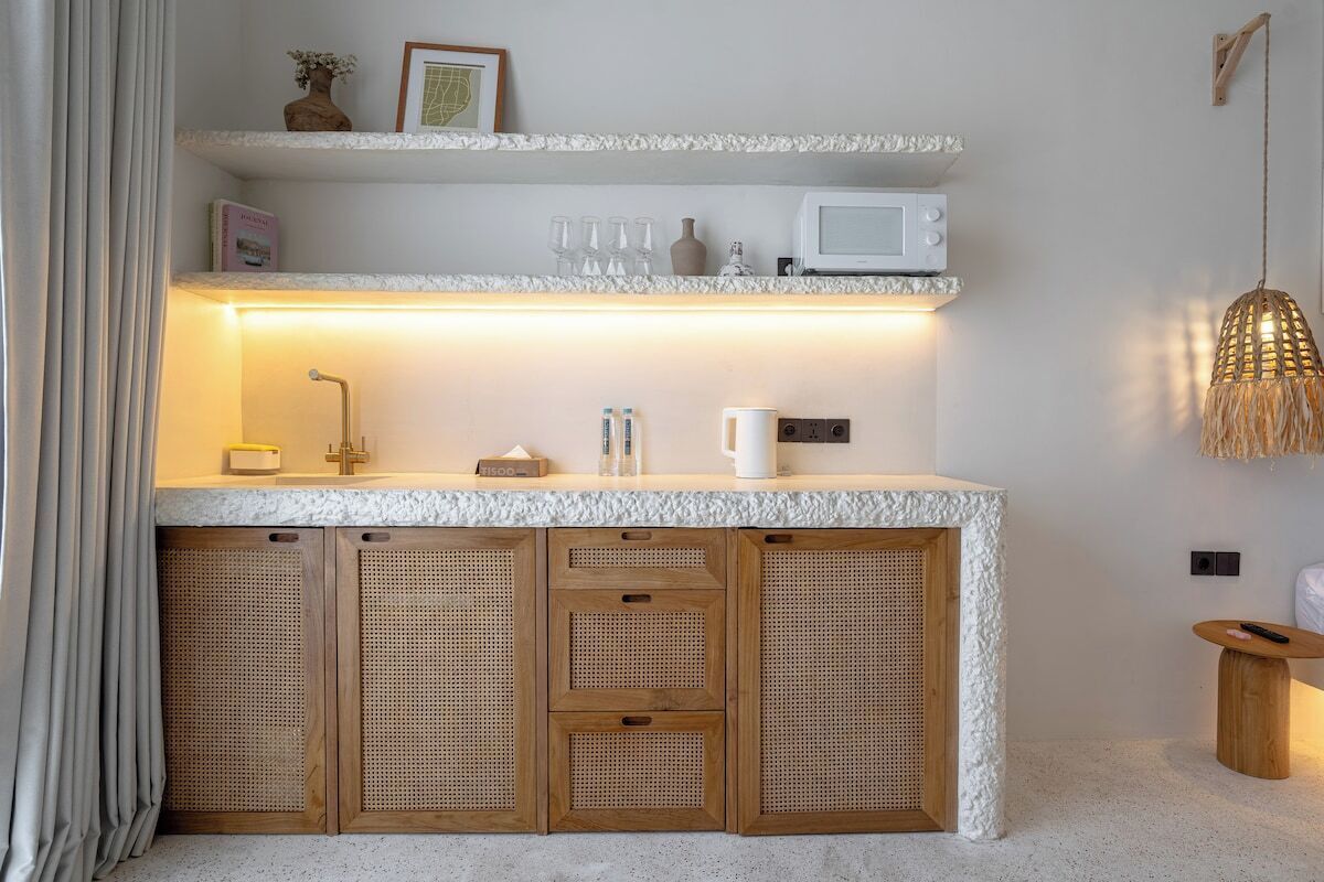 A kitchenette with a microwave, a coffee maker, and a shelf with glasses and a vase.