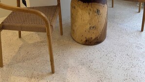 A round table with a marble top, surrounded by two wooden chairs with woven seats. A small wooden box with a tissue is placed on the table. - Brand New Apartments in Sanur+500m to Ocean+Pool (Kota Denpasar)